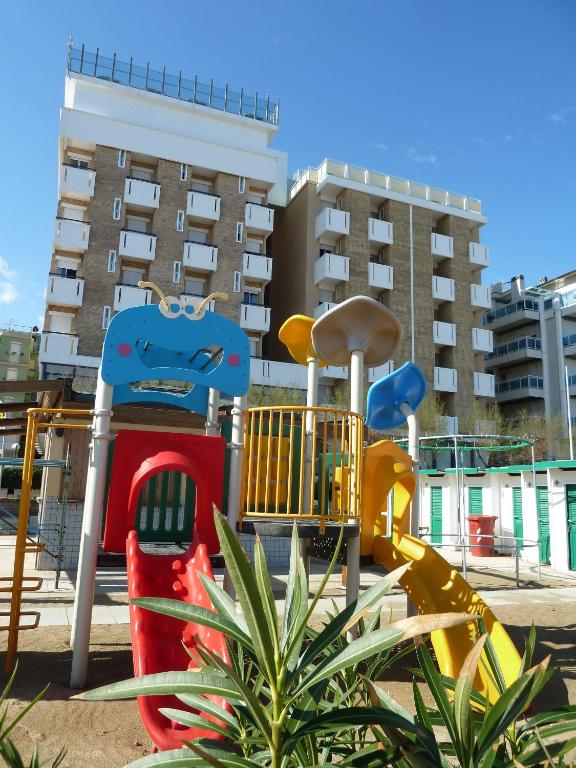 Bērnu laukums ar krāsainiem slidkalniņiem un rotaļu iekārtām, fons ar modernām ēkām.