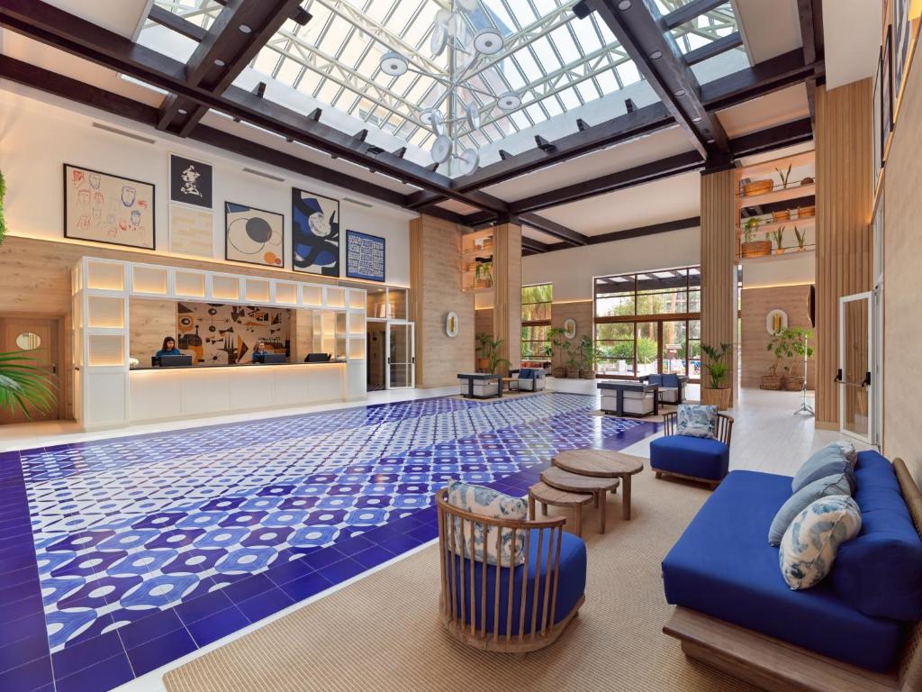 Mūsdienīgs viesnīcas vestibilis ar plašu telpu, izsistām flīzēm un mākslas darbiem uz sienām. Gaismas plūsma caur stikla jumtu piešķir telpai dzīvīgumu un siltumu.