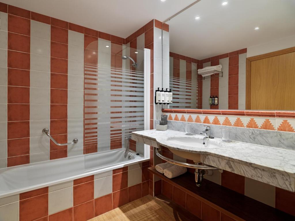 Mūsdienīga vannas istaba ar sarkanu un baltu flīžu dizainu, vannu un dušu. Aprīkota ar marmora izlietni un higiēnas piederumiem.