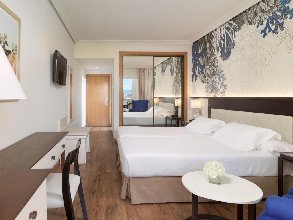 Mūsdienīga viesnīcas istaba ar divām gultām, rakstāmgaldu un atpūtas zonu. Sienas rotā eleganta ziedu tapete, un ir liels spogulis, kas paplašina telpu.