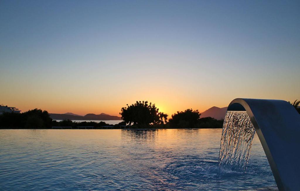 Vasaras saulriets pie baseina ar ūdens strūklu un kalnu fonu, radot mierīgu un relaksējošu atmosfēru.