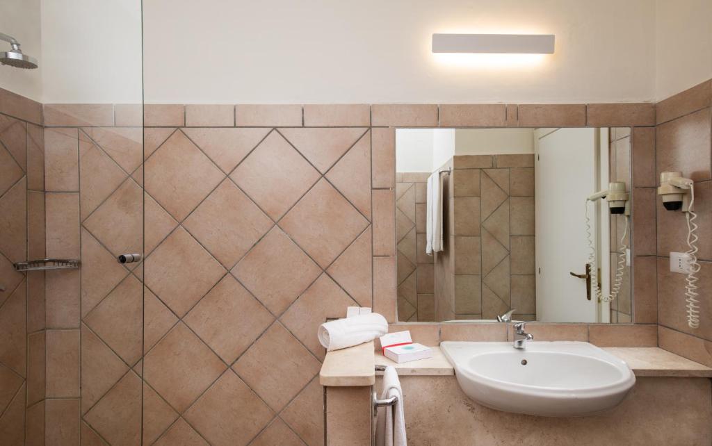 Mūsdienīgs vannas istabas interjers ar stikloto dušu, flīzētām sienām un modernu izskatu. Uz izlietnes novietoti dvieļi un higiēnas priekšmeti.