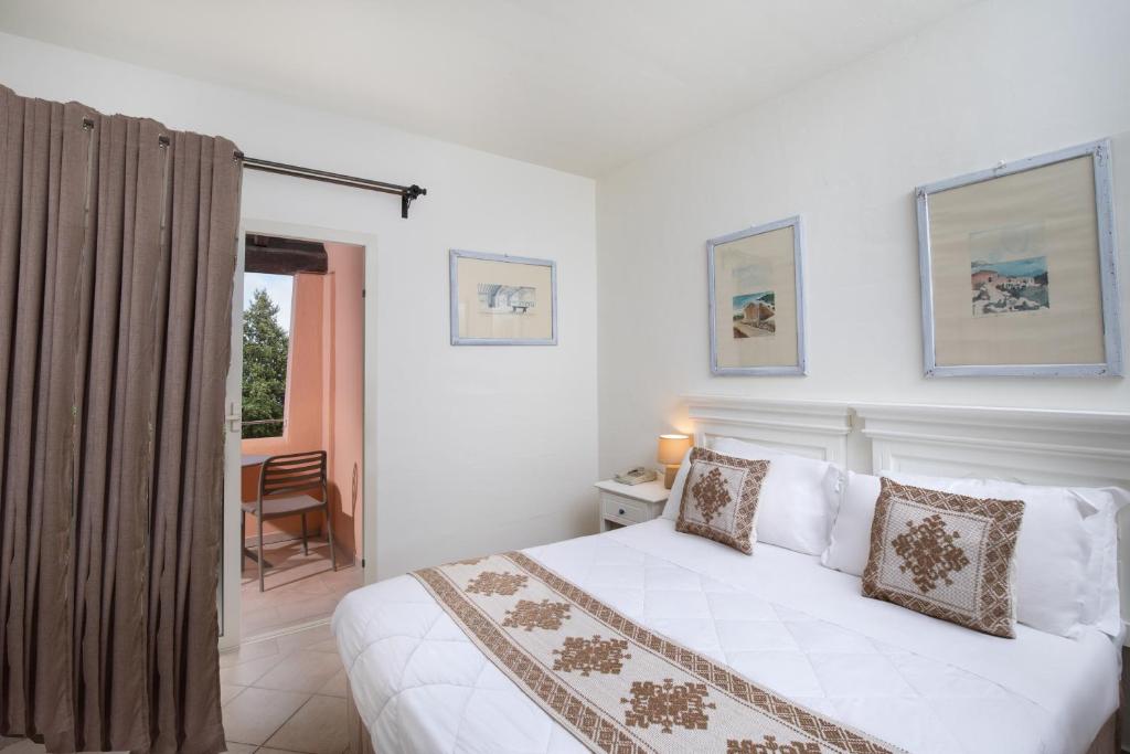 Mūsdienīga guļamistaba ar baltu gultu un dekoratīvām spilveniem, dekorēta ar ainavu gleznām, logu uz balkonu un bēšu aizkariem.