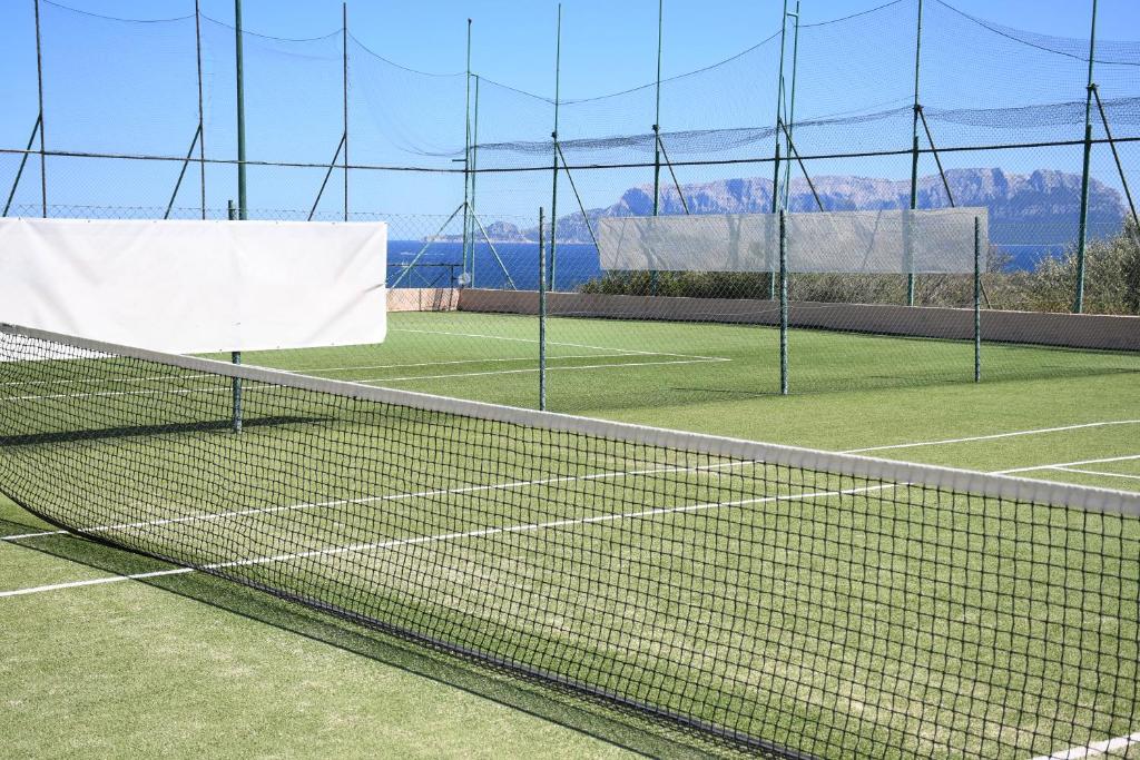 Tenisa laukums ar mākslīgo zāli, aplīmēts ar tīklu un redzama jūras ainava fona. Ideāla vieta sporta aktivitātēm un atpūtai.