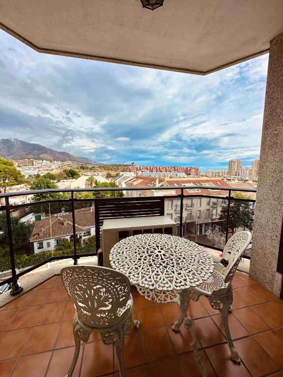 Skats no balkona uz pilsētu ar kalniem fona. Uz balkona atrodas eleganta dzelzs galds un divas krēsli, radot ideālu vietu relaksācijai.