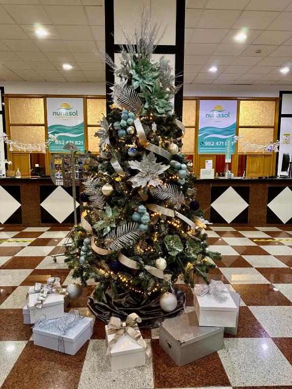 Ziemassvētku eglīte ar rotājumiem un dāvanām apakšā, izvietota viesnīcas vestibila zonā. Egle ir dekorēta ar zeltītām un sudrabotām detaļām, radot svētku atmosfēru.