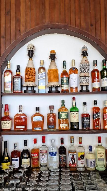 Alkohola pudeļu plaukts ar dažādām zīmolu pudelēm, tostarp viskijiem un degvīniem, rotāts ar tradicionāliem dekoriem.
