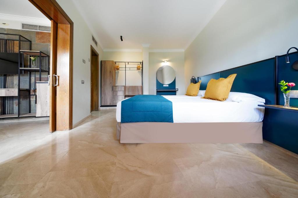 Mūsdienīgs viesnīcas numurs ar divguļamo gultu, dekorētām spilveniem un elegantu interjeru. Telpā ir gaiša krāsa, koka elementi un stilīgs apgaismojums, radot komfortablu atmosfēru.