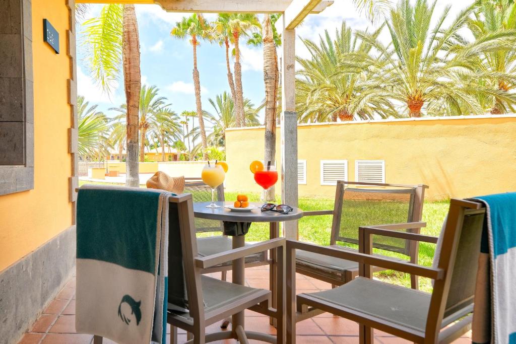 Terases skats ar palmām, divām kokteiļu glāzēm un atpūtas krēsliem, ideāli piemērots relaksācijai. Gaisīga atmosfēra un saulains laiks veicina brīvdienu sajūtu.