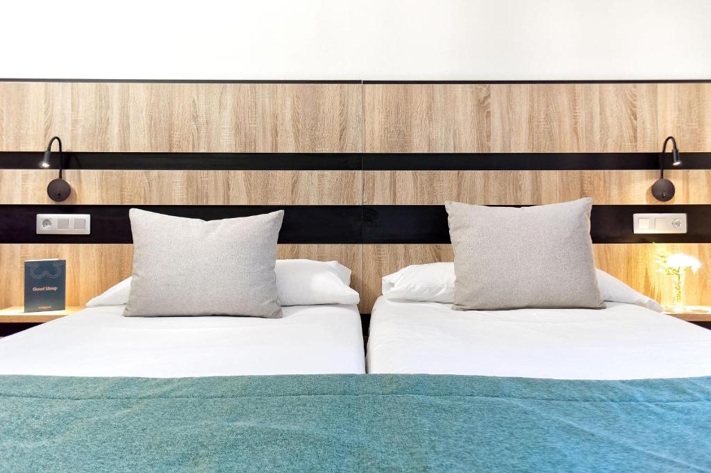 Mūsdienīgs viesnīcas numurs ar divām gultām, greznu koka apdari un mīkstiem spilveniem. Uz galda redzama grāmata "Good Sleep" un gaisma, kas rada patīkamu atmosfēru.