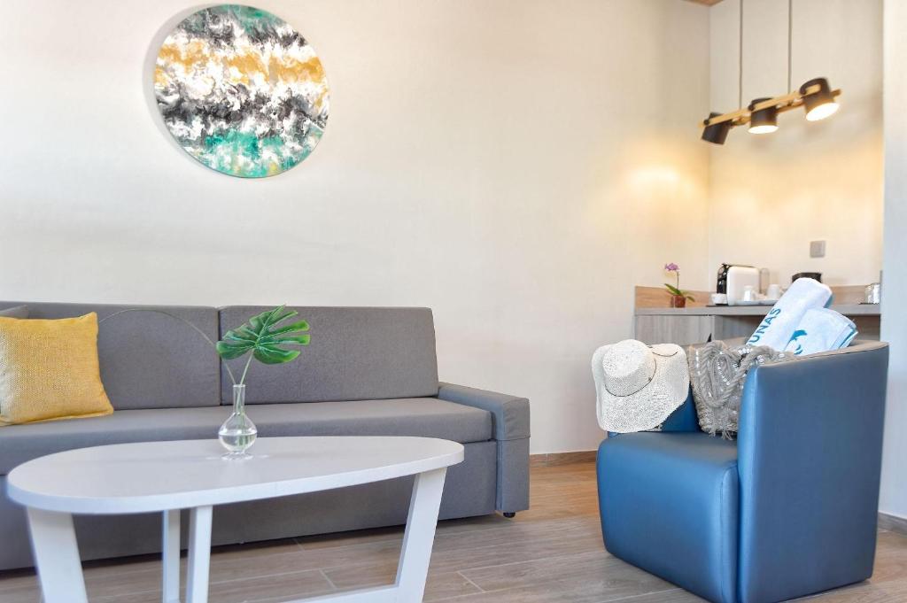 Mūsdienīgs viesistabas interjers ar pelēku dīvānu, baltu galdu un krēslu, dekorētu ar mākslas darbu pie sienas un ziedu kompozīciju. Šī telpa ir gaumīga un komfortabla, ideāli piemērota relaksācijai.