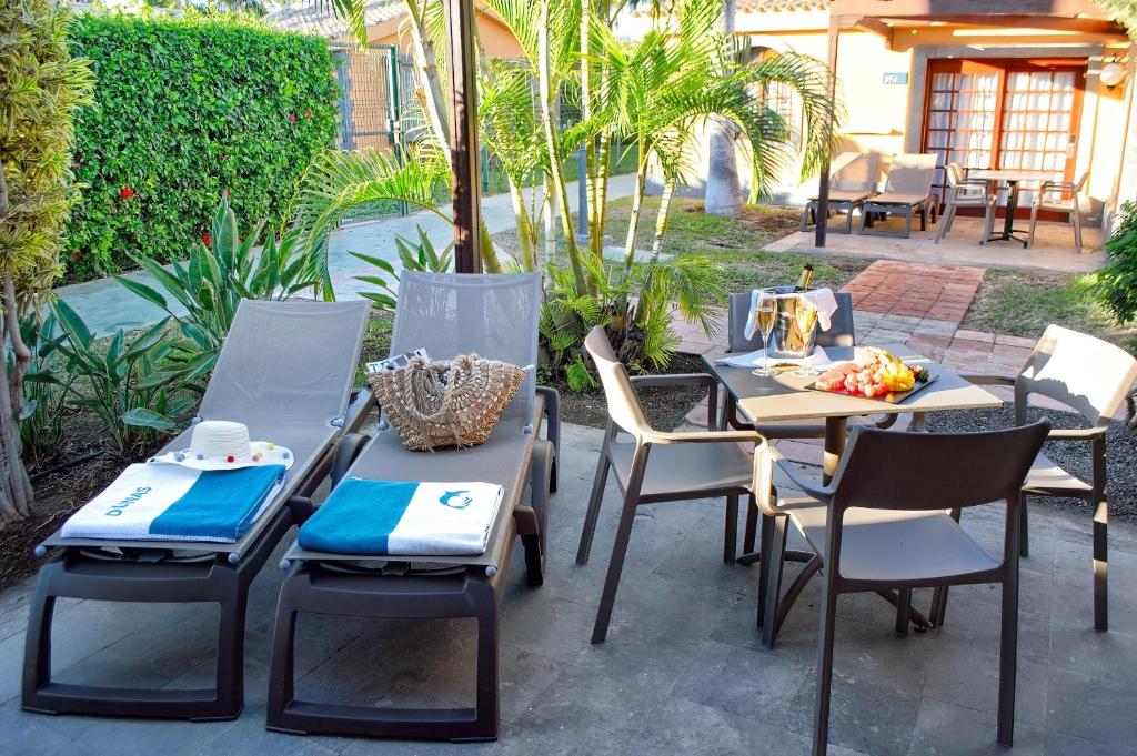 Lieliska atpūtas zona ar sauļošanās krēsliem, galdu un krēsliem, kas apņem zaļo dārzu. Uz galda ir augļu plate un šampanietis, radot relaksējošu atmosfēru.