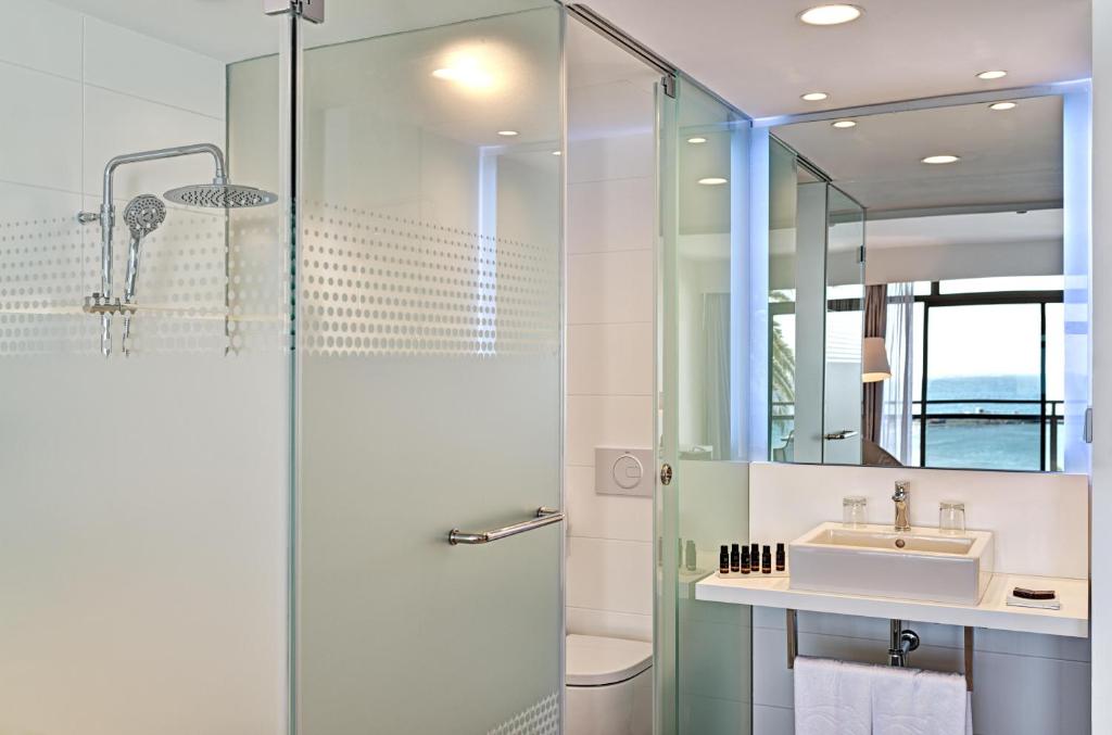 Mūsdienīgs vannas istabas interjers ar stikla dušu, elegantu izlietni un skatu uz jūru. Apgaismojums rada patīkamu atmosfēru.