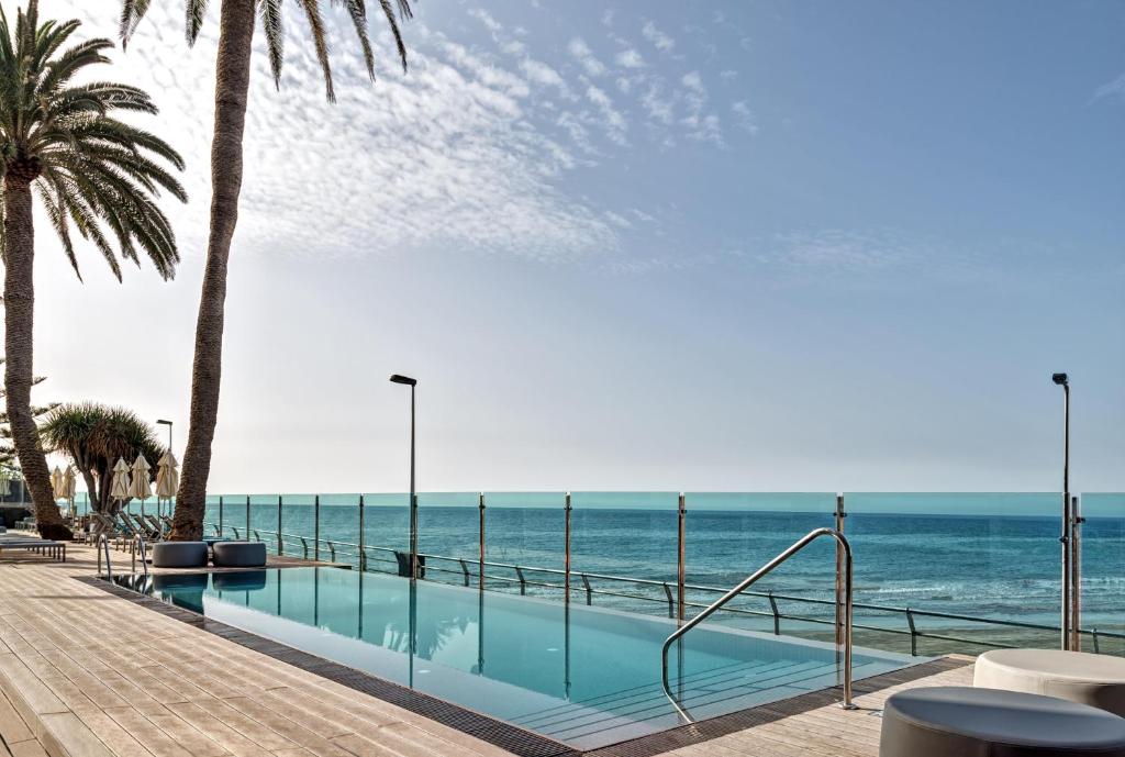 Eleganta baseina zona ar palmām un skatu uz jūru, kas rada relaksējošu atmosfēru. Ideāli piemērota atpūtai un saulē.