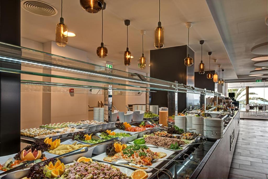 Bagātīgs bufetes galda piedāvājums ar dažādiem salātiem, augļiem un ēdieniem modernā restorānā. Apgaismojums rada siltu atmosfēru.