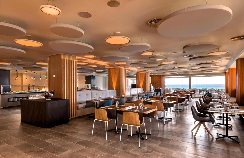 Moderns restorāns ar elegantu interjeru, kurā ir koka mēbeles un stilīgi gaismas avoti. Logi piedāvā skatu uz jūru, radot patīkamu atmosfēru.