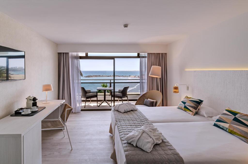 Mūsdienīgs viesnīcas numurs ar divām gultām, skatu uz jūru, kafejnīcas stūri un ērtu atpūtas zonu. Interjers ir gaišs un elegants, radot relaksējošu atmosfēru.