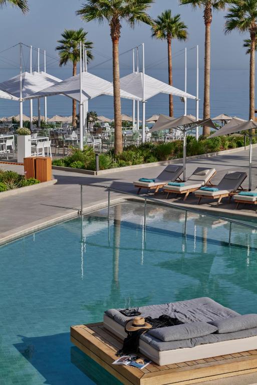 Eleganta peldbaseina zona ar palmām un sauļošanās krēsliem, kas piedāvā relaksāciju un atpūtu pie ūdens. Fons ietver modernu terasi un jūras ainavu, radot ideālu atmosfēru brīvdienām.