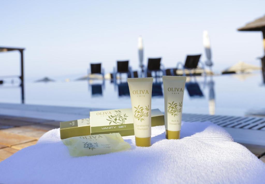 Kosmētikas komplekts "Oliva" ar šampūnu un dušas želeju, izvietots pie baseina. Fons ar peldēšanas krēsliem un saulainu debesu ainavu.