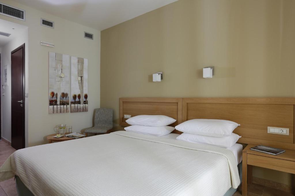 Mūsdienīga viesnīcas numura iekārtojums ar divguļamo gultu, gaismas piekari un dekoratīviem attēliem uz sienām. Numurā ir arī komfortabla krēsla un galda zona.