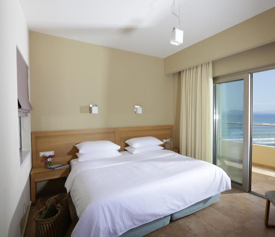 Moderns guļamistaba ar divvietīgu gultu, gaiši toņi un plaša terase ar skatu uz jūru. Interjers ir minimālisma stilā, ar dabisku apgaismojumu.