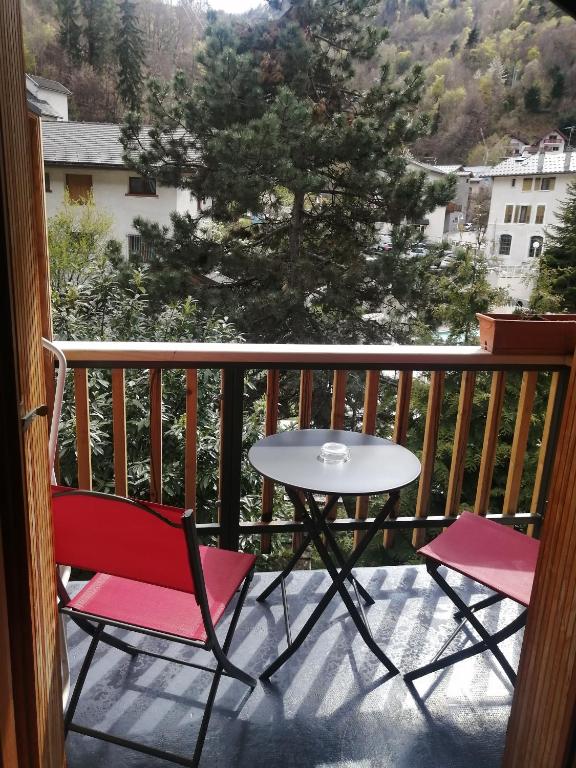 Balkons ar divām sarkanām krēslām un apaļu galdu, kas piedāvā skatu uz zaļiem kokiem un tuvējiem mājokļiem. Daba un atpūta harmonijā.