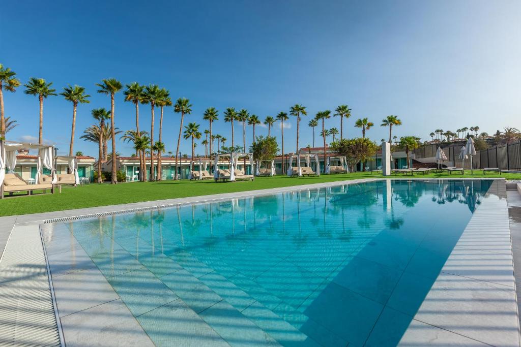 Luksusa viesnīcas baseins ar palmām un atpūtas zonu, kas piedāvā ideālu vietu relaksācijai saulainā dienā.