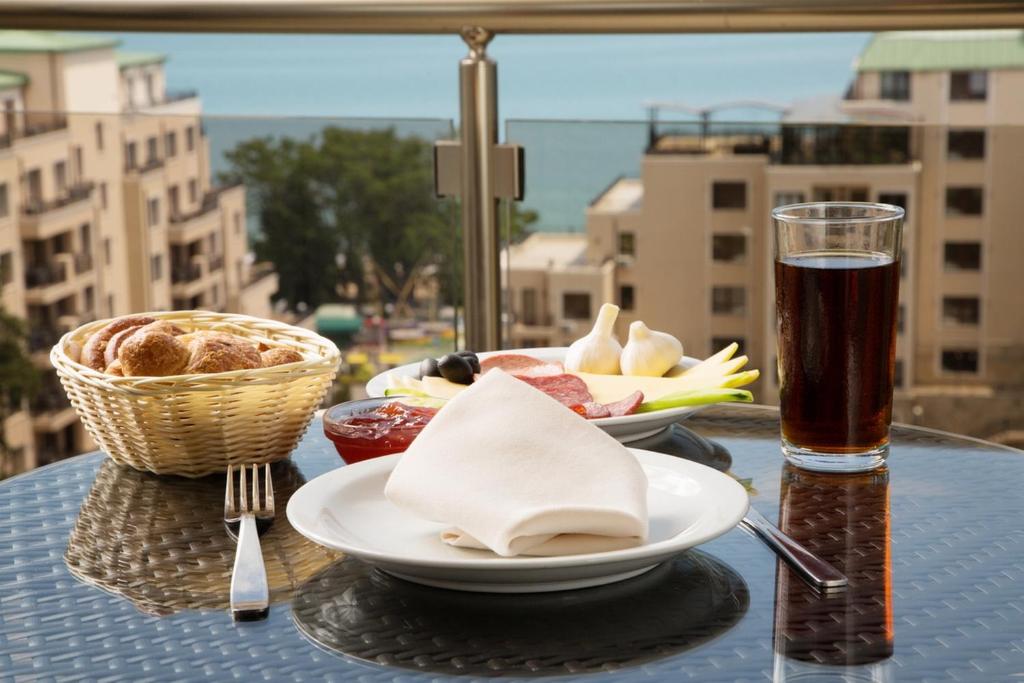 Brokastis uz balkona ar skatu uz jūru, pasniegtas ar maizēm, gaļu, dārzeņiem un dzērienu.