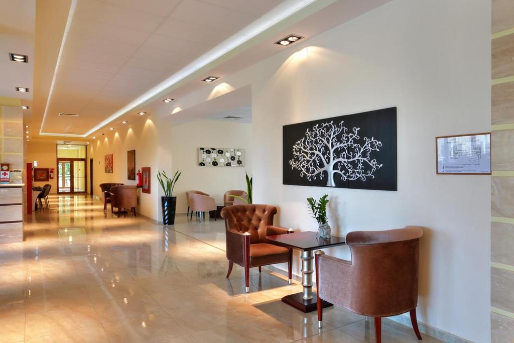 Mūsdienīgs viesnīcas vestibilis ar elegantiem dīvāniem, mākslas darbiem uz sienām un dabas elementiem. Telpa ir gaiša un aicinoša, radot patīkamu atmosfēru apmeklētājiem.