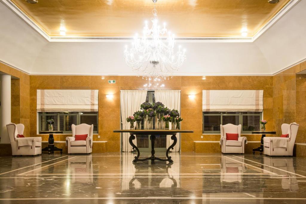 Elegants viesnīcas vestibils ar greznu lustru, mājīgu galdu un ērtām krēsliem, kas izrotāti ar ziediem. Interjera dizains apvieno modernus un klasiskus elementus.