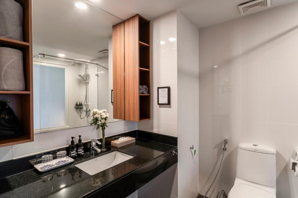 Mūsdienīgs vannas istabas interjers ar melnu akmens izlietni, koka plauktiem un dušu ar stikla durvīm. Telpā ir arī ziedi, higiēnas piederumi un eleganta apgaismojuma sistēma.