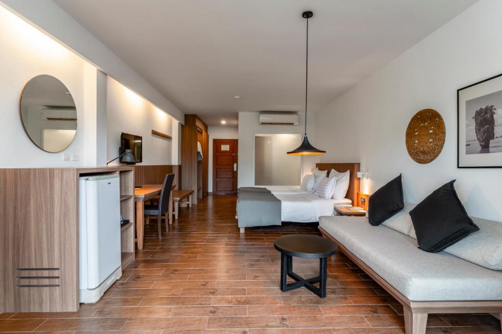 Mūsdienīga viesnīcas istaba ar koka grīdu, ērtu dīvānu, galdu, televizoru un ledusskapi. Telpā ir gaismas elementi un mākslas darbi, radot patīkamu atmosfēru.