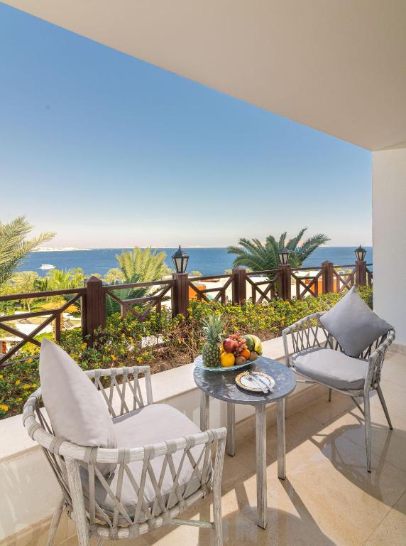 Balcony with a stunning sea view, featuring two elegant chairs and a table adorned with fresh fruits, surrounded by lush greenery and palm trees.