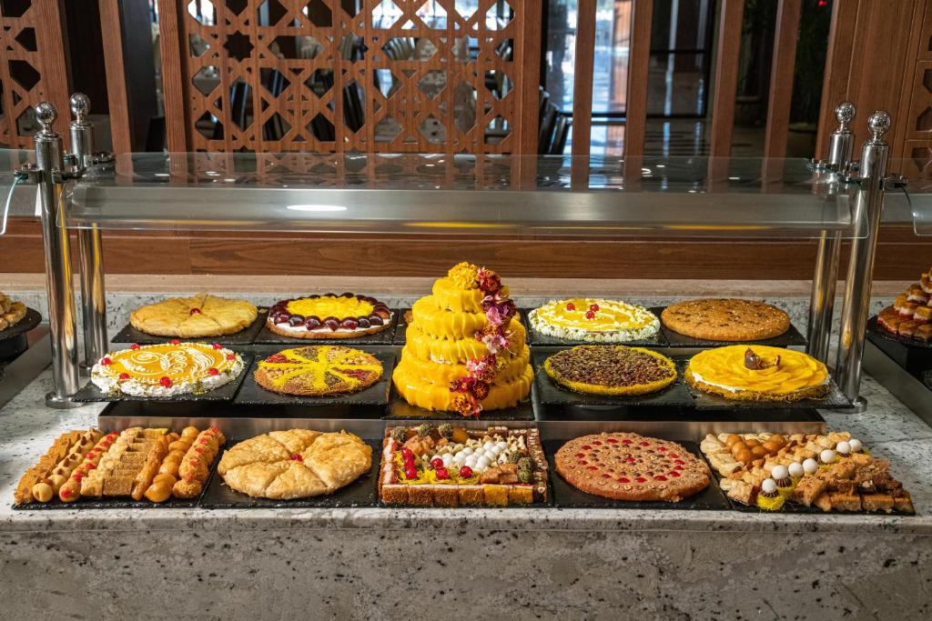 Deserts izkārtojums ar dažādām kūkām un saldumiem, tostarp krāsainām tortēm un tradicionālajiem konditorejas izstrādājumiem. Šī saldā izstāde ir pievilcīga un piedāvā plašu izvēli.
