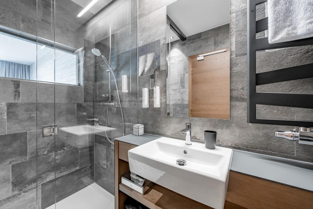 Mūsdienīgs vannas istabas interjers ar stikla dušas kabīni, elegantām flīzēm un minimālistisku izskatu. Izceļas baltā izlietne un koka akcenti.