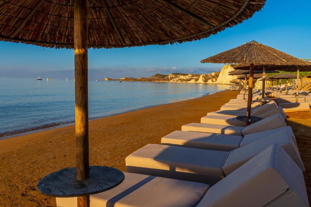 Pludmales skats ar sauļošanās krēsliem un pļavu, fona klintis un mierīgu jūru. Ideāla vieta relaksācijai un atpūtai.