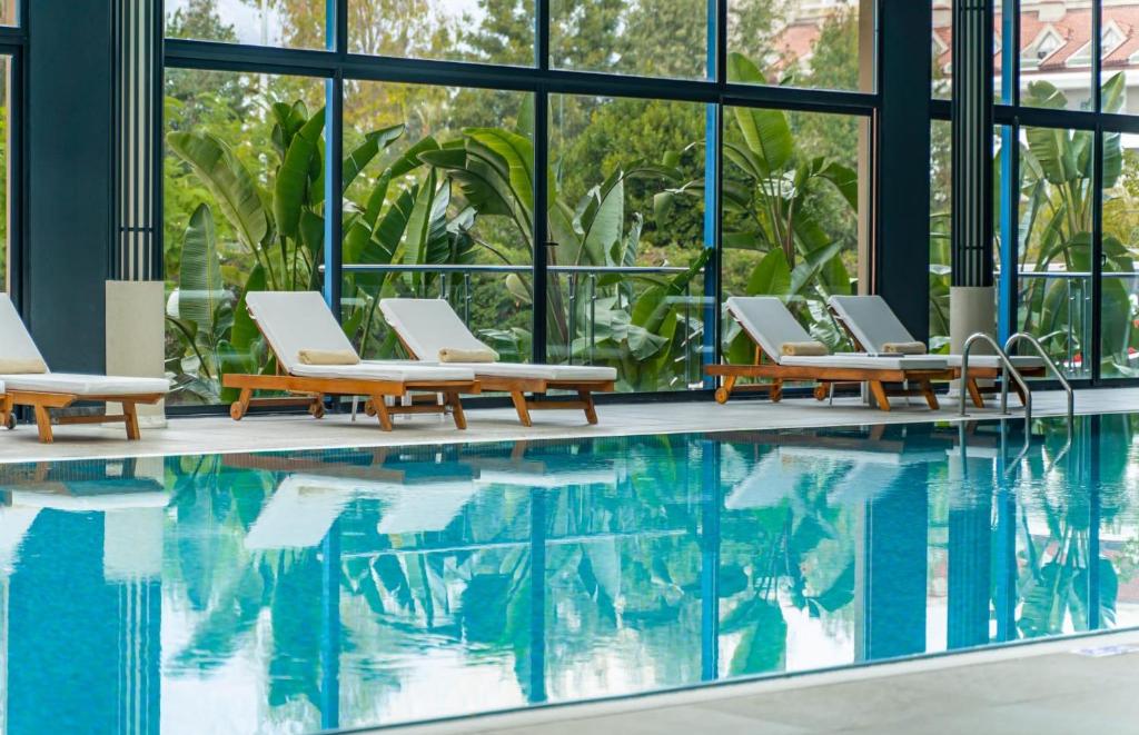 Mirage Park Resort iekštelpu baseins ar sauļošanās krēsliem un zaļām augu ainavām.