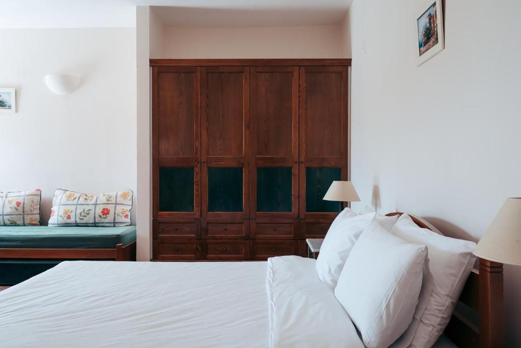 Mūsdienīgs guļamistabas interjers ar koka skapjiem, ērtu gultu un dekoratīvu dīvānu. Gaismas toņi un dabīgi elementi rada relaksējošu atmosfēru.