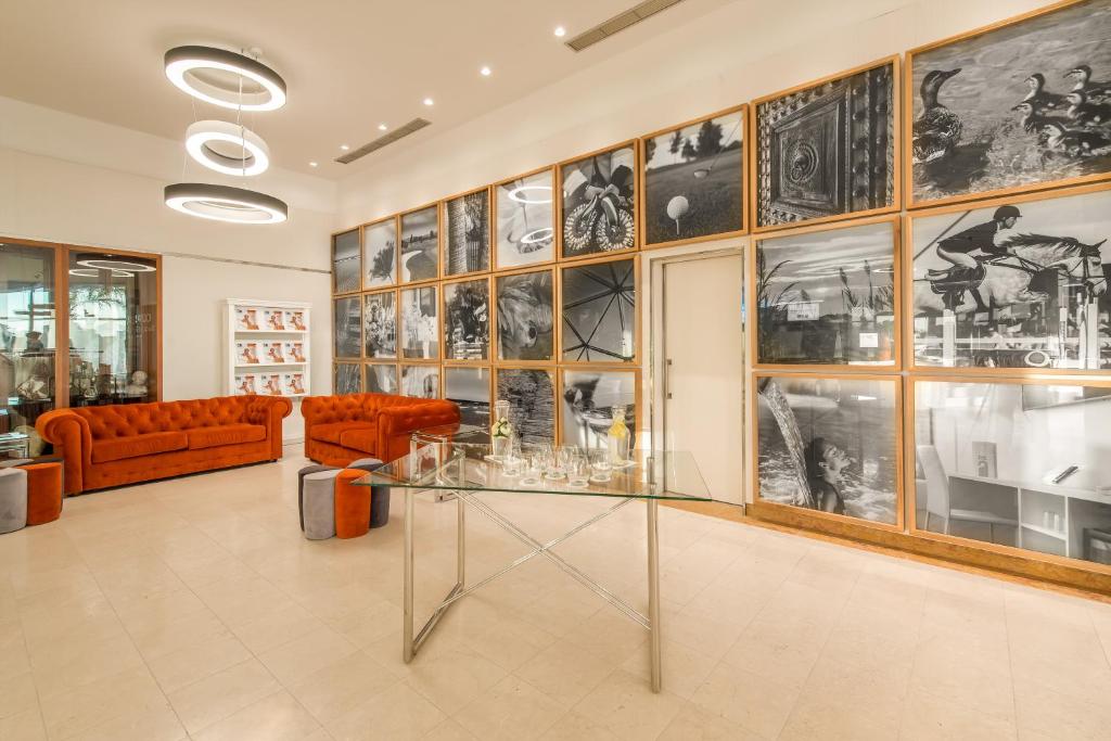 Mūsdienīgs interjers ar oranžiem dīvāniem, stilīgu stikla galdu un melnbaltām fotogrāfijām uz sienas. Telpa izskatās eleganta un viesmīlīga.