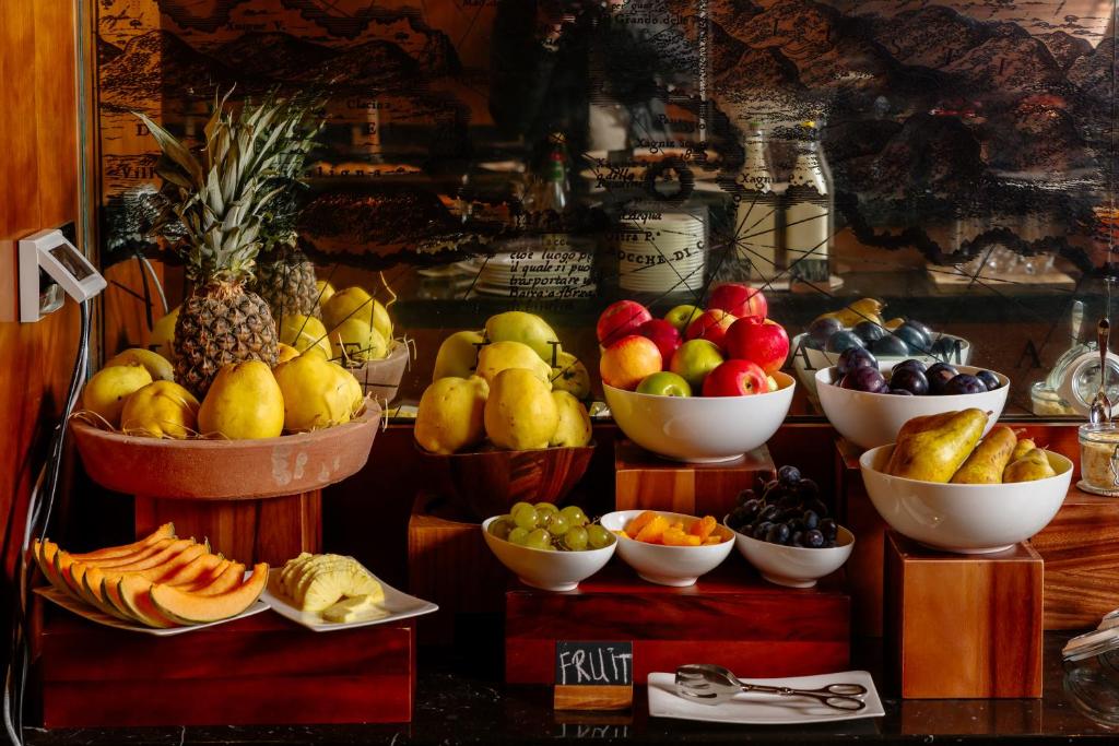 Krāšņs augļu bufete ar dažādiem augļiem, tostarp ananāsiem, bumbieriem, āboliem, vīnogām un arbūziem, izkārtoti eleganti uz koka plauktiem.