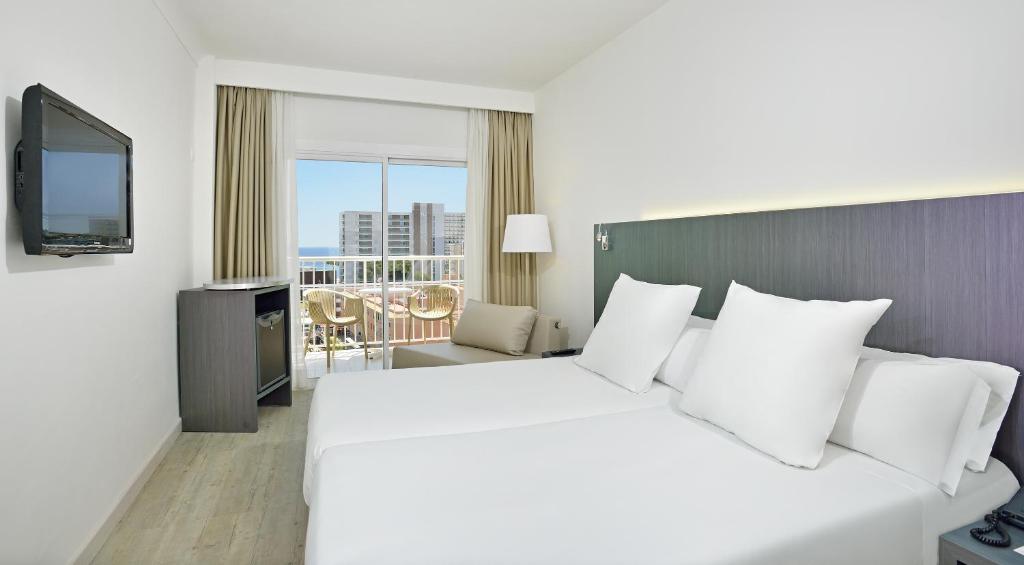 Moderns viesnīcas numurs ar divām gultām, televizoru un skatu uz jūru. Interjers ir gaišs un minimālistisks, ar koka grīdu un ērtu atpūtas zonu.