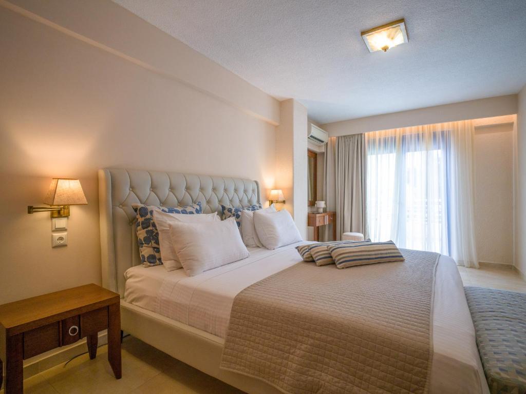 Mūsdienīgs guļamistabas interjers ar ērtu gultu, dekoratīvām spilveniem un lieliem logiem, caur kuriem plūst dabiska gaisma. Telpa ir iekārtota ar vienkāršām mēbelēm un siltām krāsām, radot mājīgu atmosfēru.