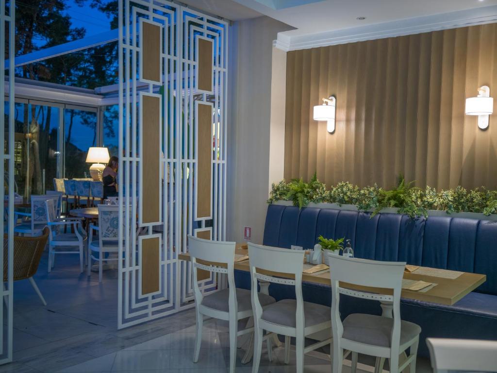 Mūsdienīgs restorāna iekšējais interjers ar elegantu dīvānu, baltām koka mēbelēm un dekoratīvām augu kompozīcijām, radot patīkamu atmosfēru.