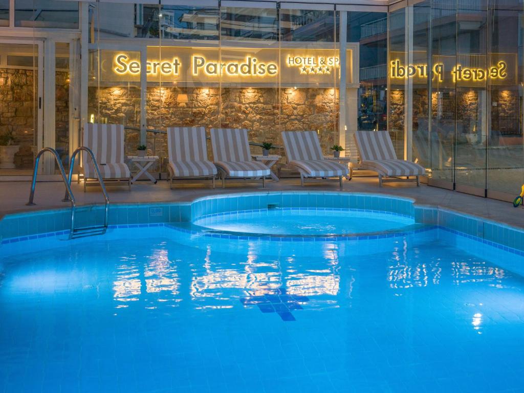 Baseins ar zilu ūdeni un atpūtas krēsliem, apgaismots ar "Secret Paradise" zīmi. Viegli moderna atmosfēra, ideāla relaksācijai.