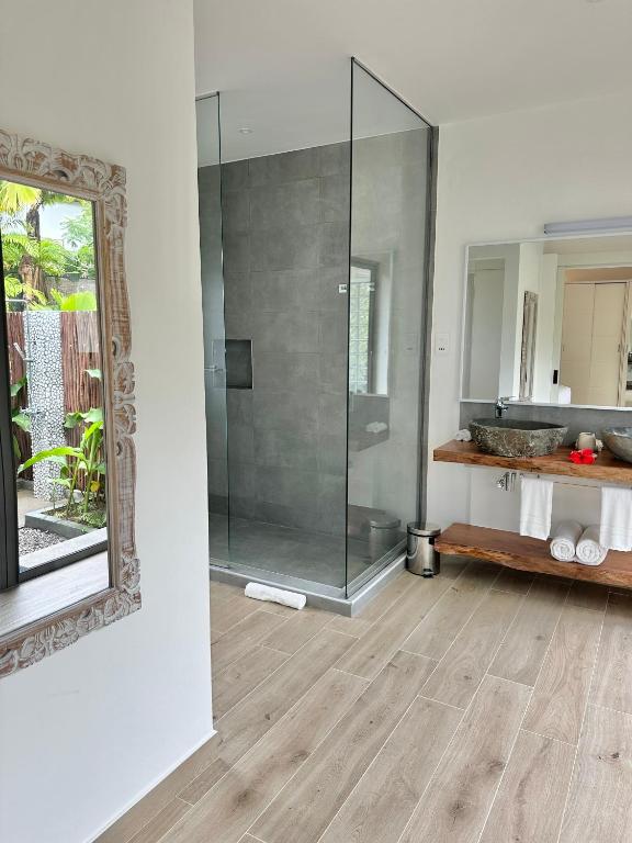 Mūsdienīgs vannas istabas interjers ar stikla dušu un dabīgu akmens izlietni, papildināts ar koka plauktu un elegantu spoguli. Izteikta gaismas un telpas harmonija.