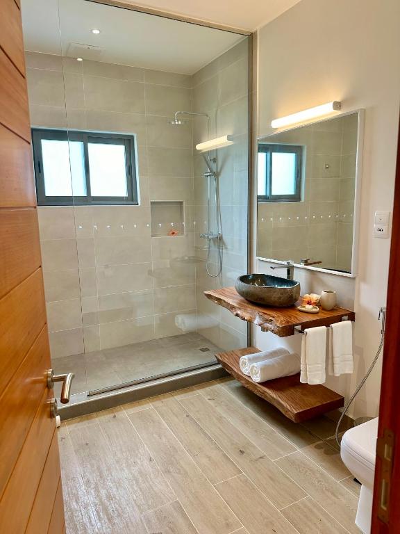 Mūsdienīga vannas istaba ar stikla dušu, koka izlietni un elegantu spoguli. Telpa ir gaiša un gaumīgi iekārtota, radot relaksējošu atmosfēru.