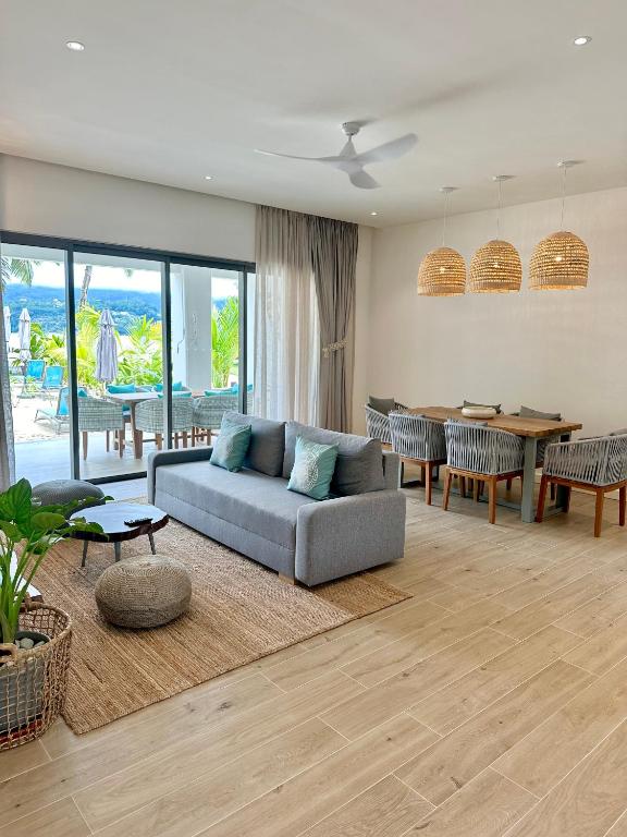 Mūsdienīga viesistaba ar pelēku dīvānu, ēdamgaldu un gaismas ķermeņiem, kas radīta relaksējošai atmosfērai. Logi ved uz āra terasi un dārzu ar baseinu.