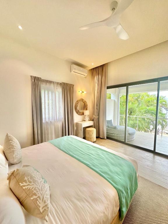 Mūsdienīga guļamistaba ar gaisīgu interjeru, kurā ir liela gulta ar zaļganu pārklāju un piekļuve balkonam, no kura paveras skats uz zaļo dabu.