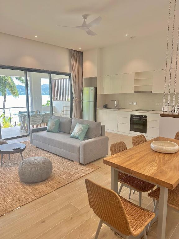 Mūsdienīgs dzīvojamās istabas interjers ar dīvānu, koka galdu un skatu uz jūru. Telpa ir gaiša un plaša, ar dabīgām koka grīdām un modernām mēbelēm.