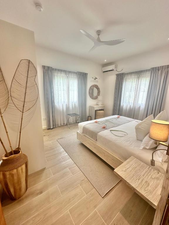 Moderns guļamistabas interjers ar gultu, dabīgiem materiāliem un gaisīgu atmosfēru. Logi ar aizkariem un dekoratīvi elementi radījuši mājīgu noskaņu.